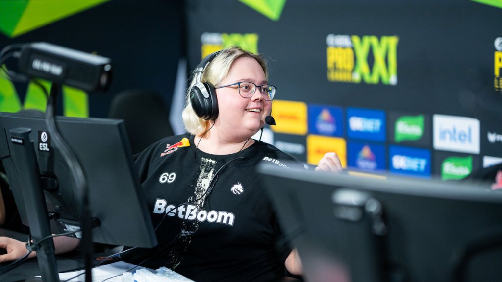 Esports player engaged in a Counter-Strike tournament, wearing a headset and sitting at a gaming setup with sponsor logos in the background.