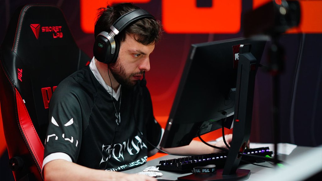 Focused esports player in a black jersey, wearing a headset, intensely gaming on a computer at a professional event