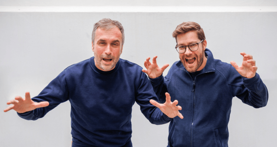 Two men in navy sweaters making playful gestures.