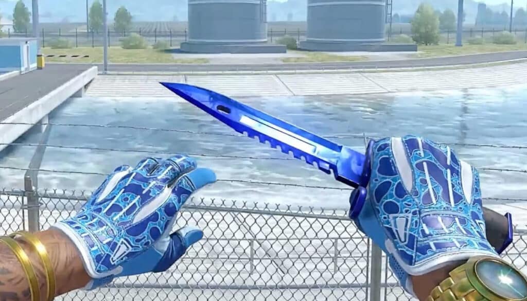 A Counter Strike player holding a vibrant blue knife with matching gloves, set in an industrial map environment.