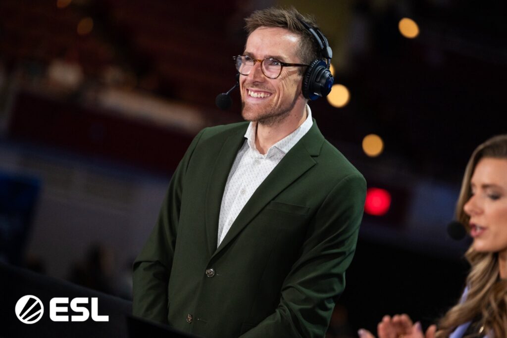 ESL commentator in a green suit speaking into a microphone during a live esports event