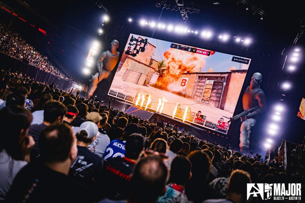 Audience watches Counter-Strike tournament on large screen at esports event, with explosive in-game action displayed.