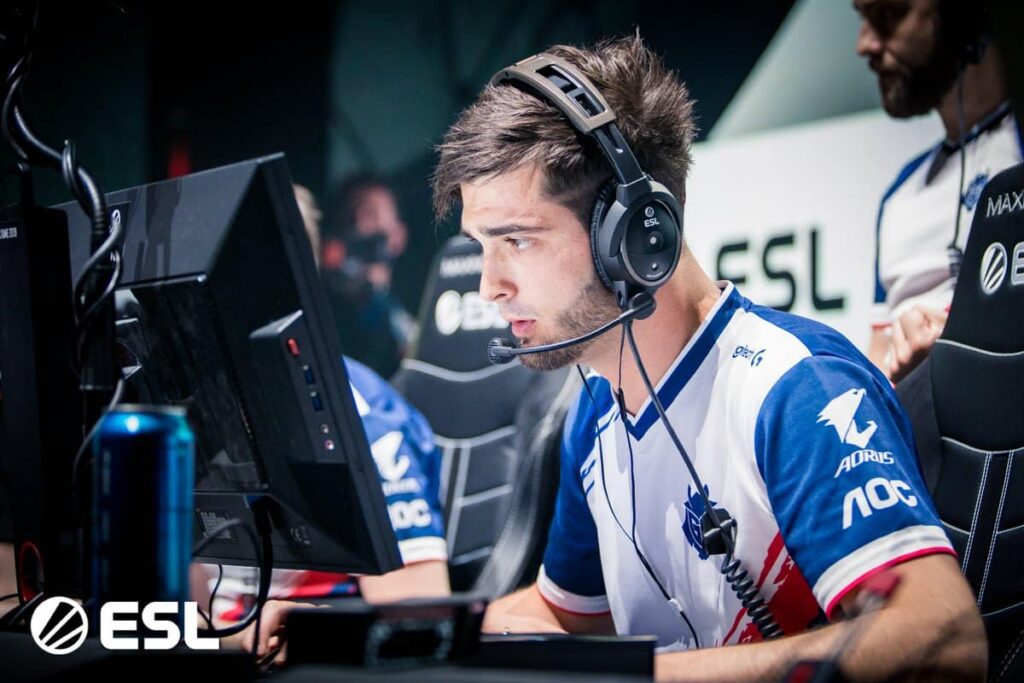 Esports player intensely focused during an ESL Counter-Strike match, wearing headphones and a team jersey.