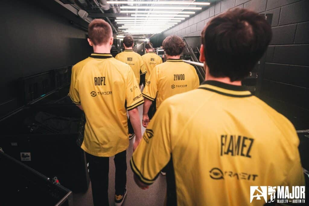 Esports team in yellow jerseys walking down a corridor at a gaming event.