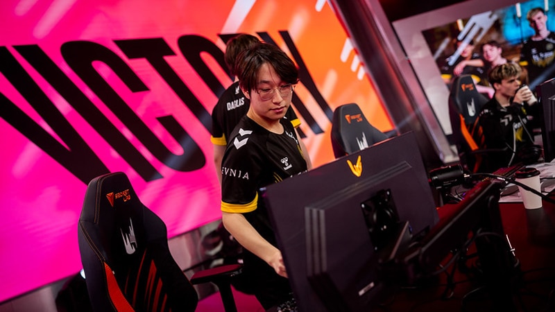 Esports player celebrating a victory at a gaming event, with bright victory sign in the background