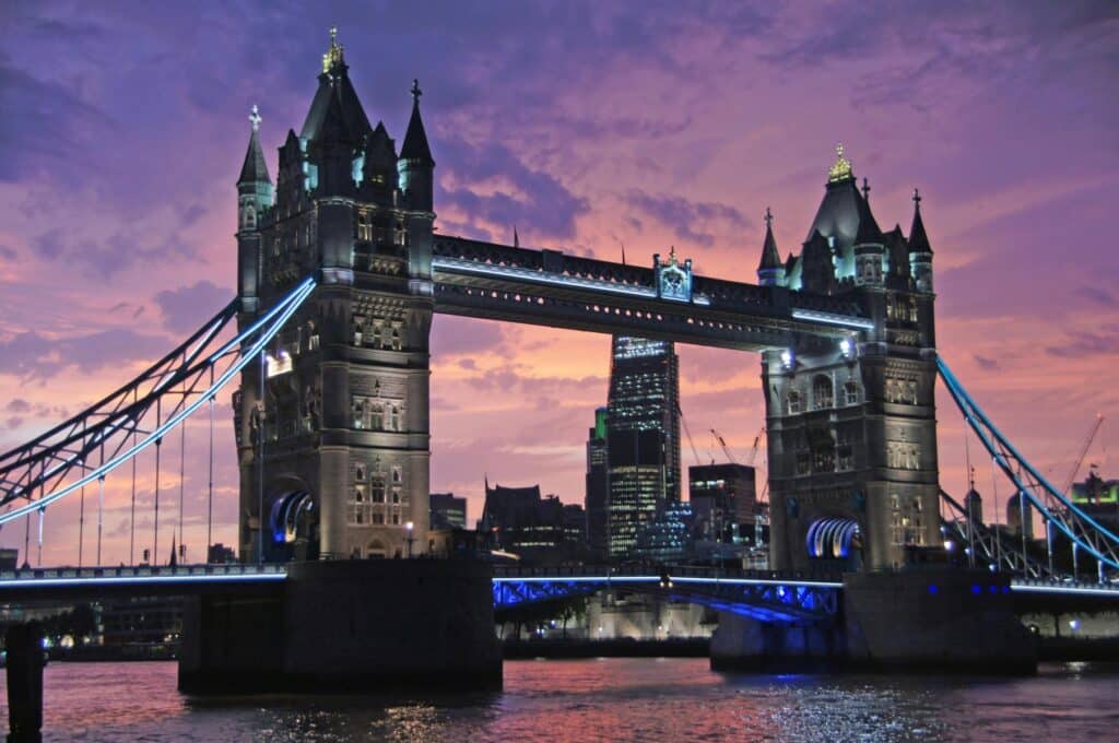 Night view of a brightly lit tower bridge against a vibrant purple and orange sky, reminiscent of immersive gaming environments.