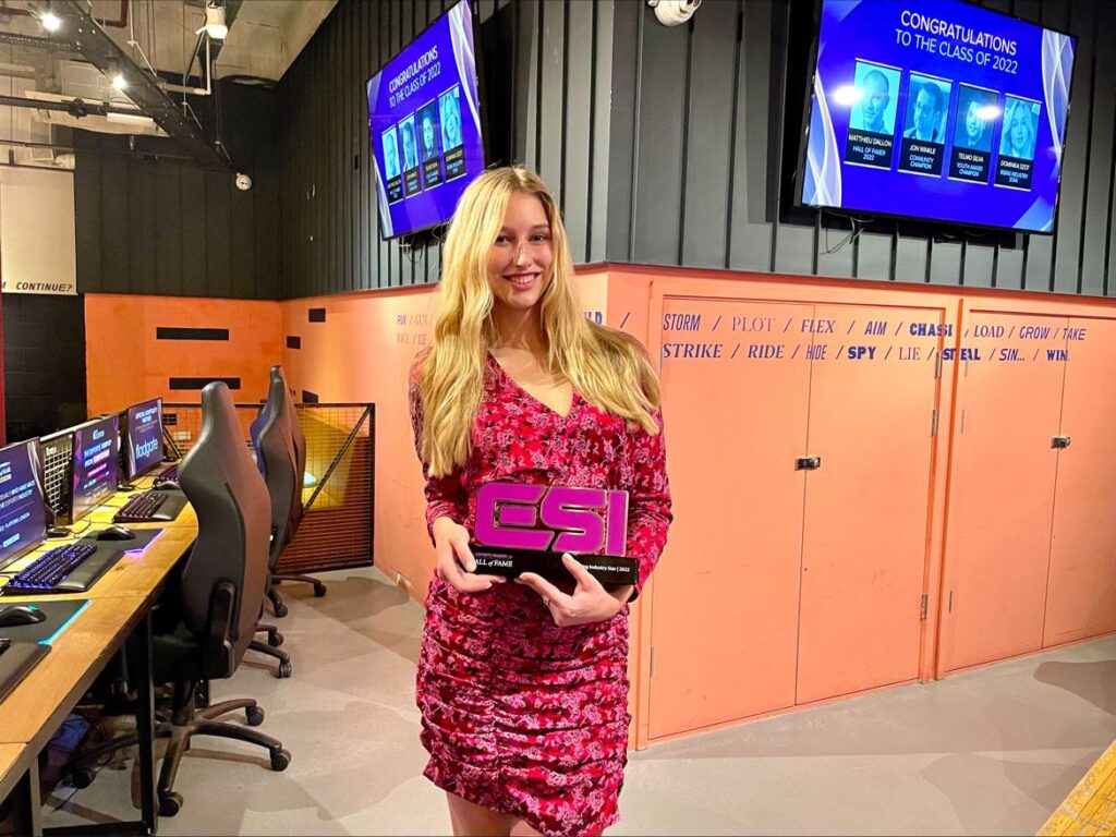 Person holding an esports award in a gaming setup with monitors and congratulatory messages