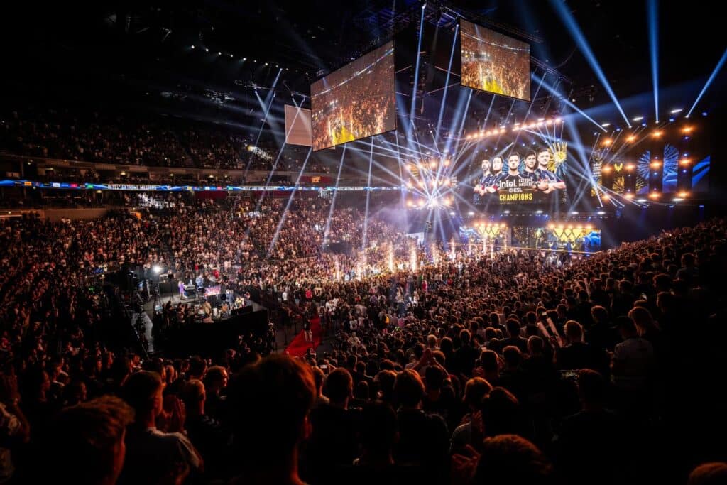 Packed esports arena with vibrant lights and large screen showing champions at a Counter-Strike event.