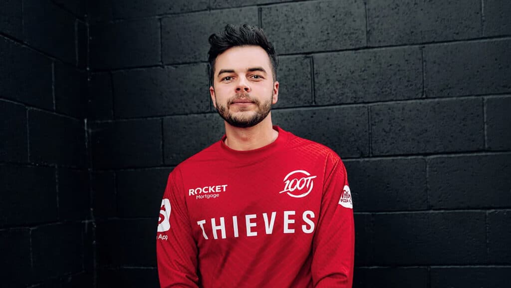Person in red 100 Thieves jersey standing against a black wall